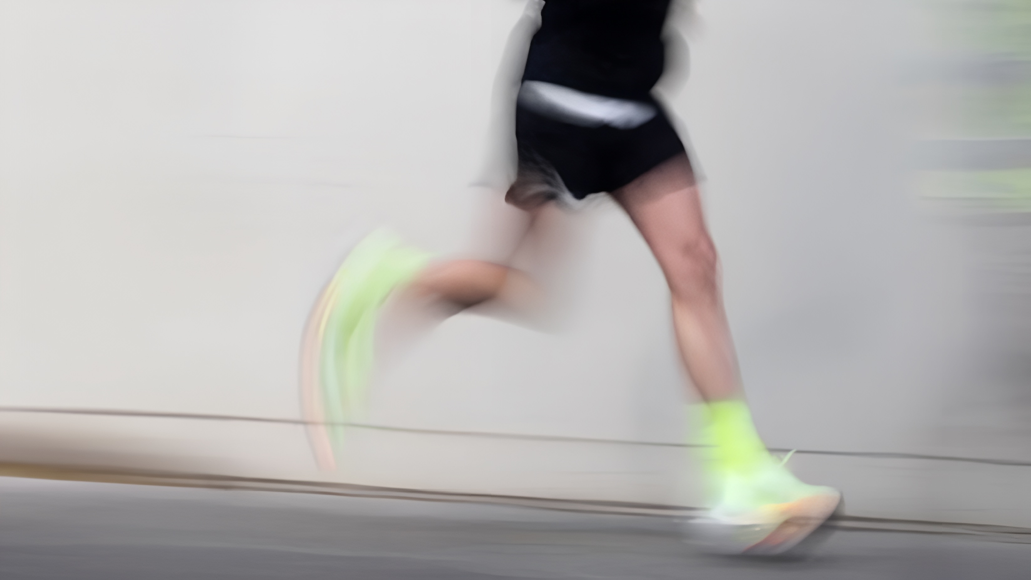 Motion-blurred photograph of a runner moving past a grey wall.