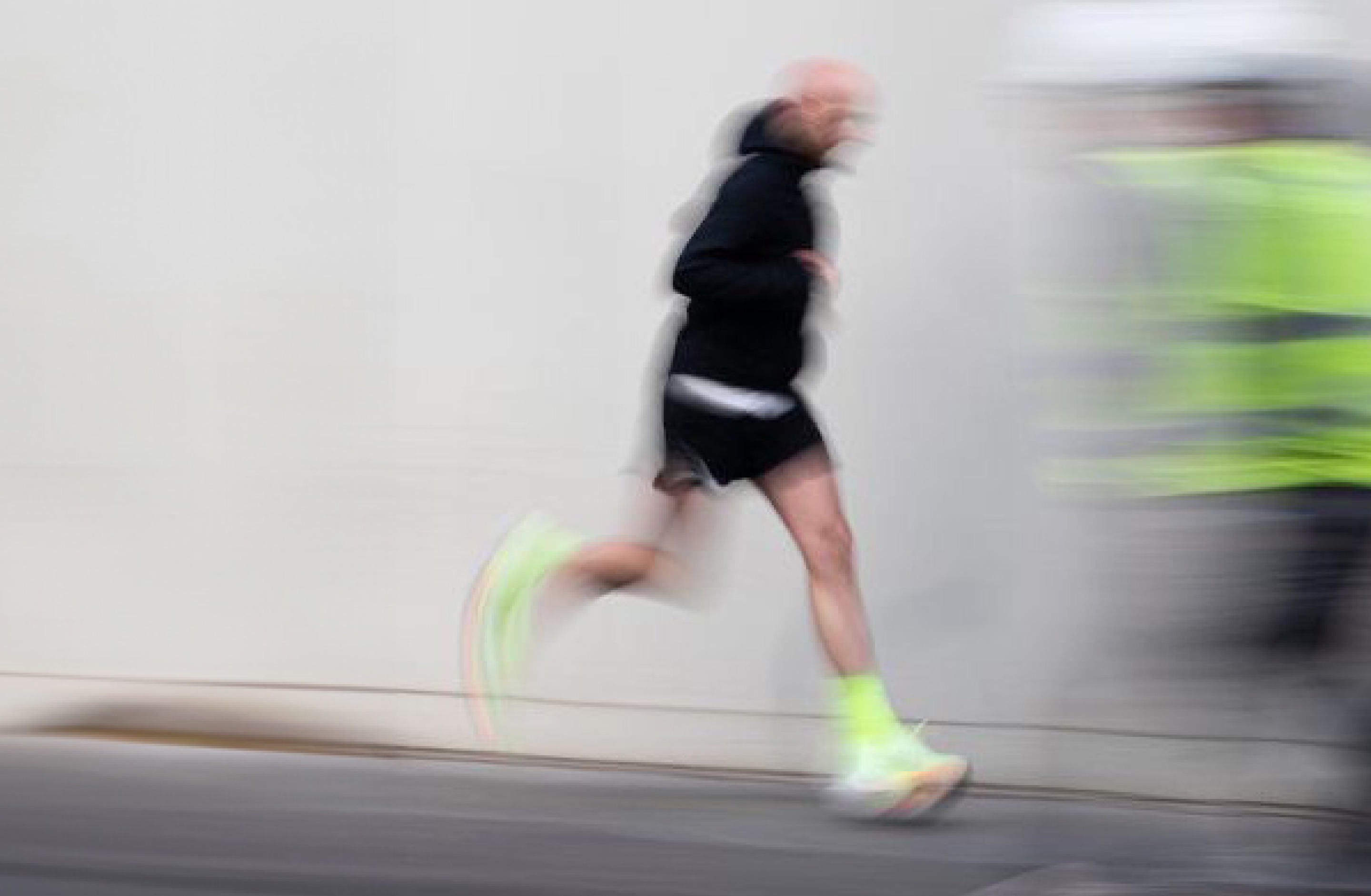 Motion-blurred photograph of a runner moving past a grey wall.